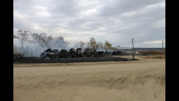 Long stacks of round hay bales across the countryside smolder in the aftermath of the Cottonwood Fire.