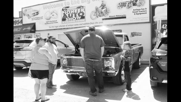 Car enthusiasts gather around this orange 1970s Chevrolet C10 pickup.